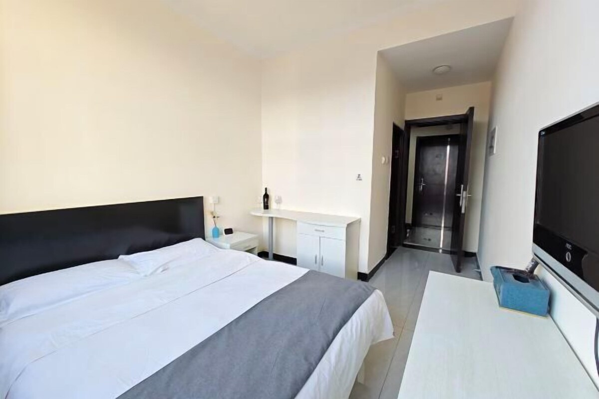 A hotel room with a bed, a desk, a television, and a door leading to a hallway.