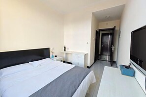 Habitación de hotel con cama, escritorio, televisor y puerta que da a un pasillo.