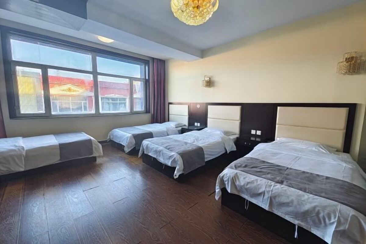 A hotel room with four beds, a large window, and a chandelier.