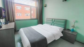 A hotel room with a bed, bedside table, and a window with curtains.
