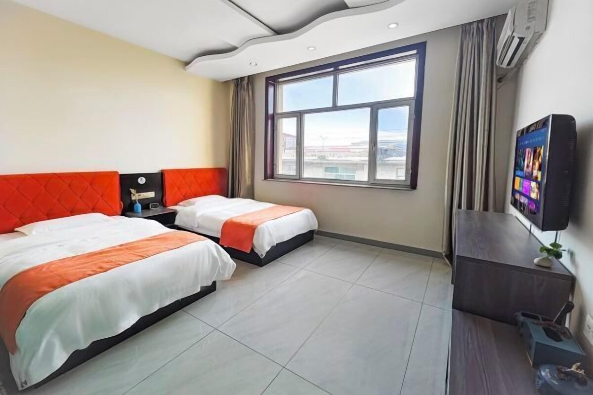 A hotel room with two beds, a TV, a desk, and a window with a city view.