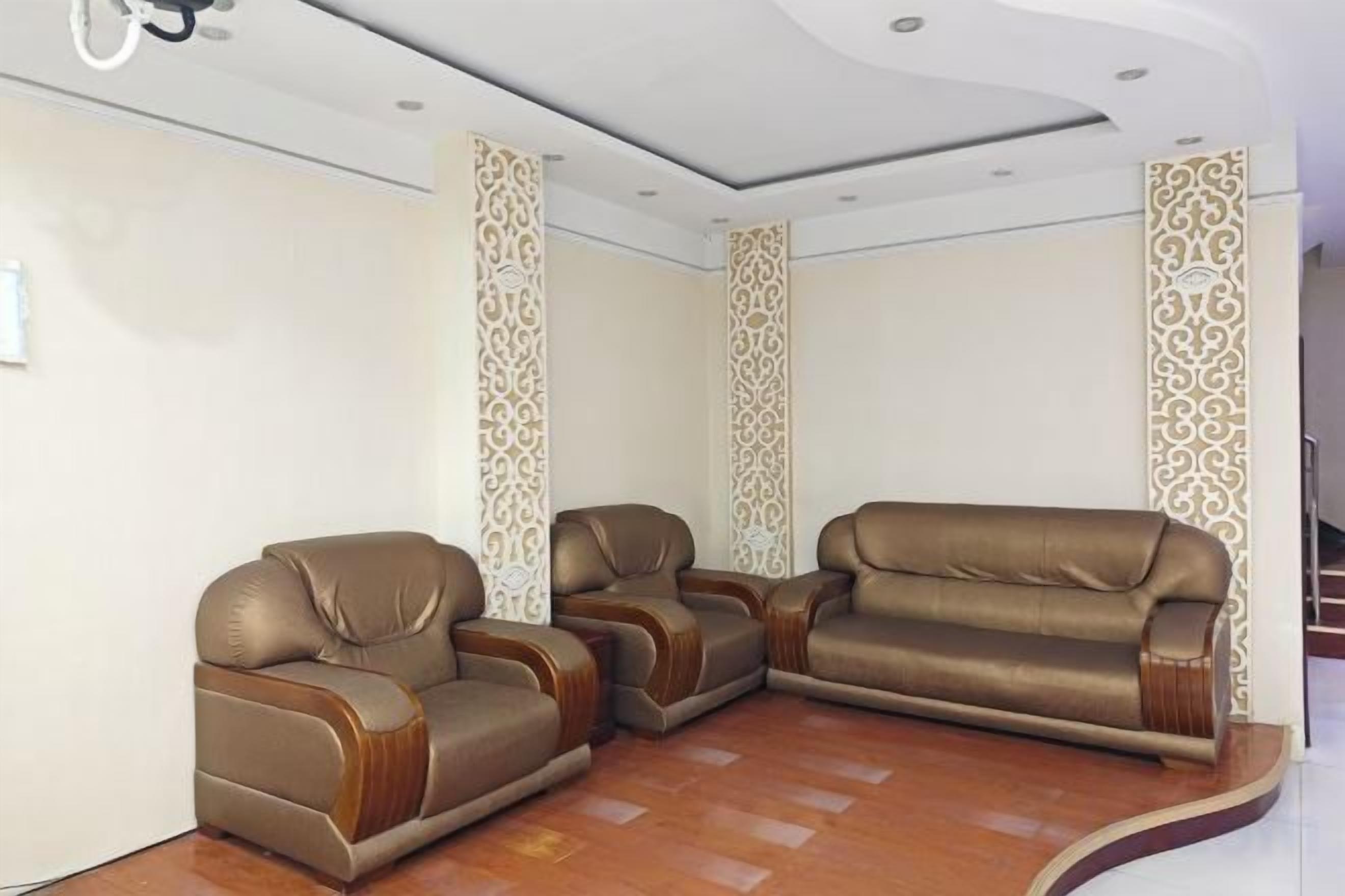 A room with three leather sofas arranged in a U-shape, a wooden floor, and decorative wall panels.