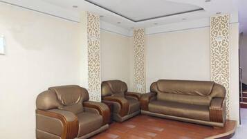 A room with three leather sofas arranged in a U-shape, a wooden floor, and decorative wall panels.