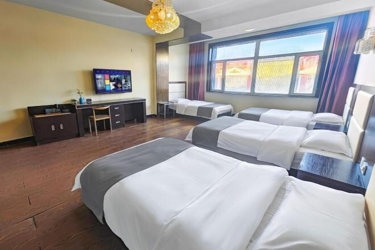 A hotel room with four beds, a desk, a TV, and a large window with curtains.