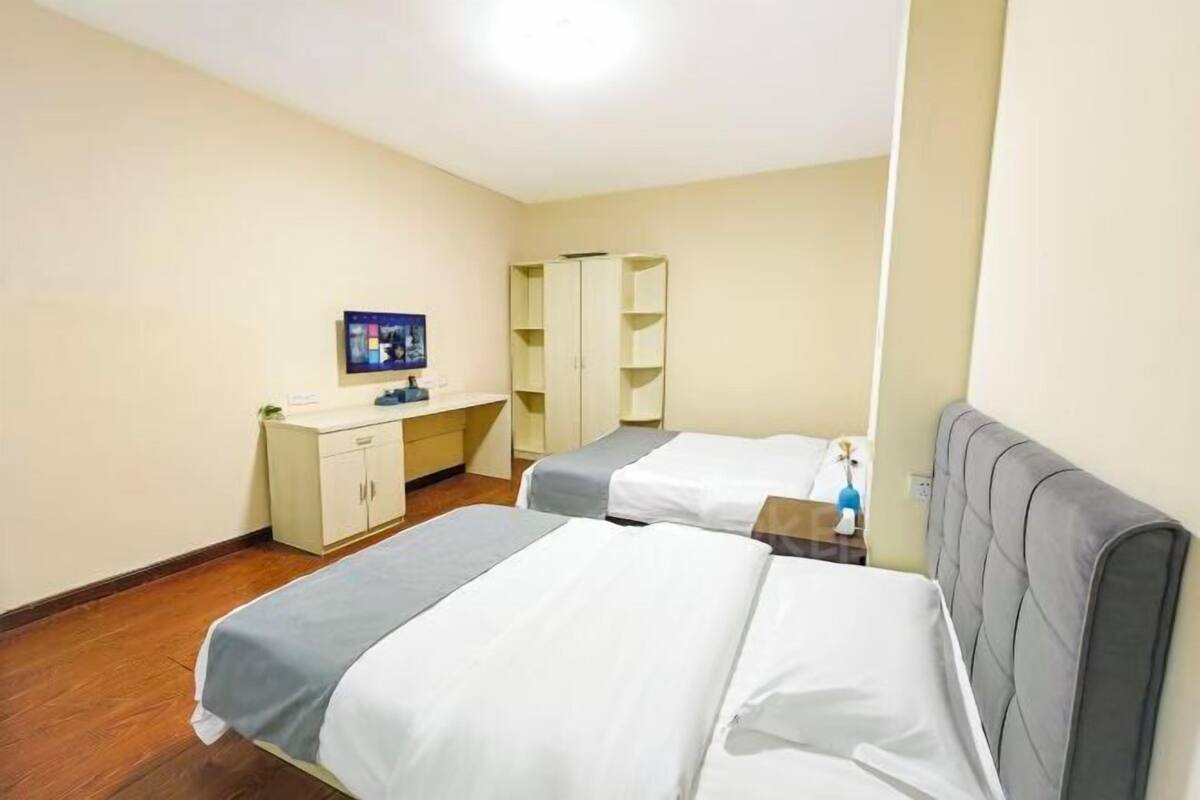 A hotel room with two beds, a desk, a wardrobe, and a television.