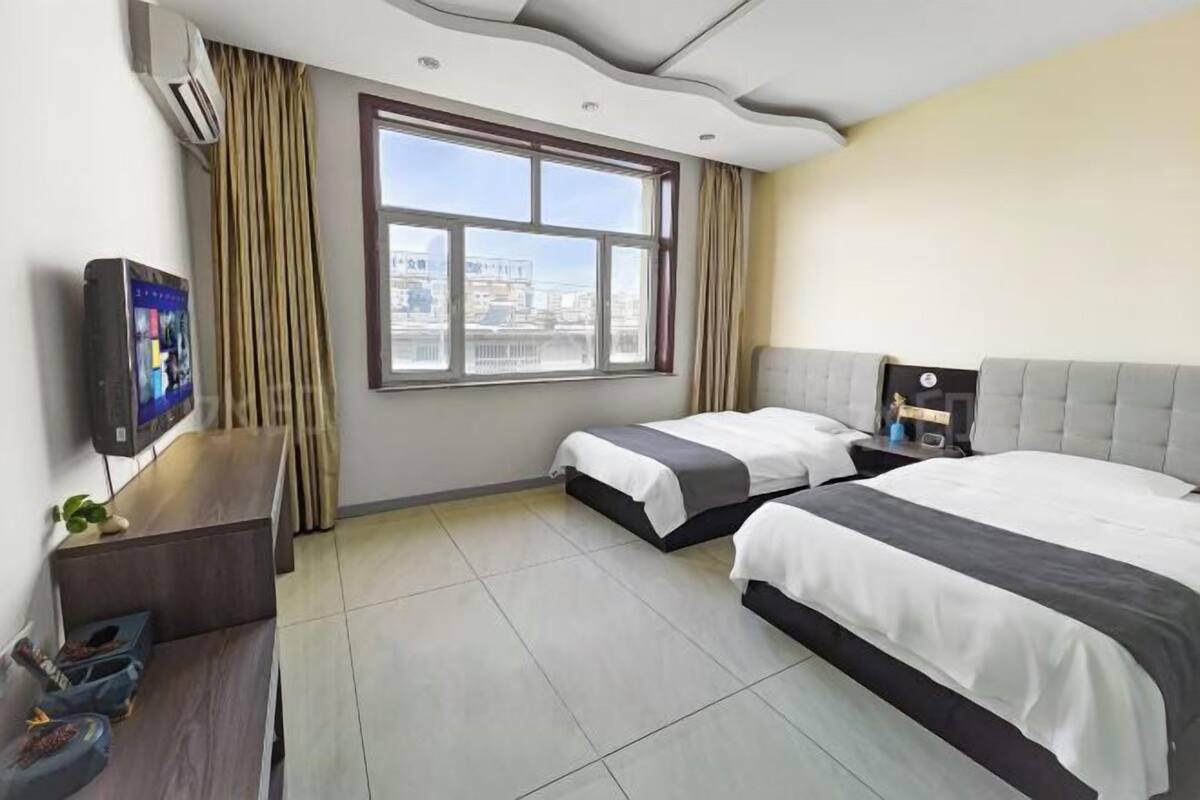 A hotel room with two beds, a TV, a desk, and a window with a city view.