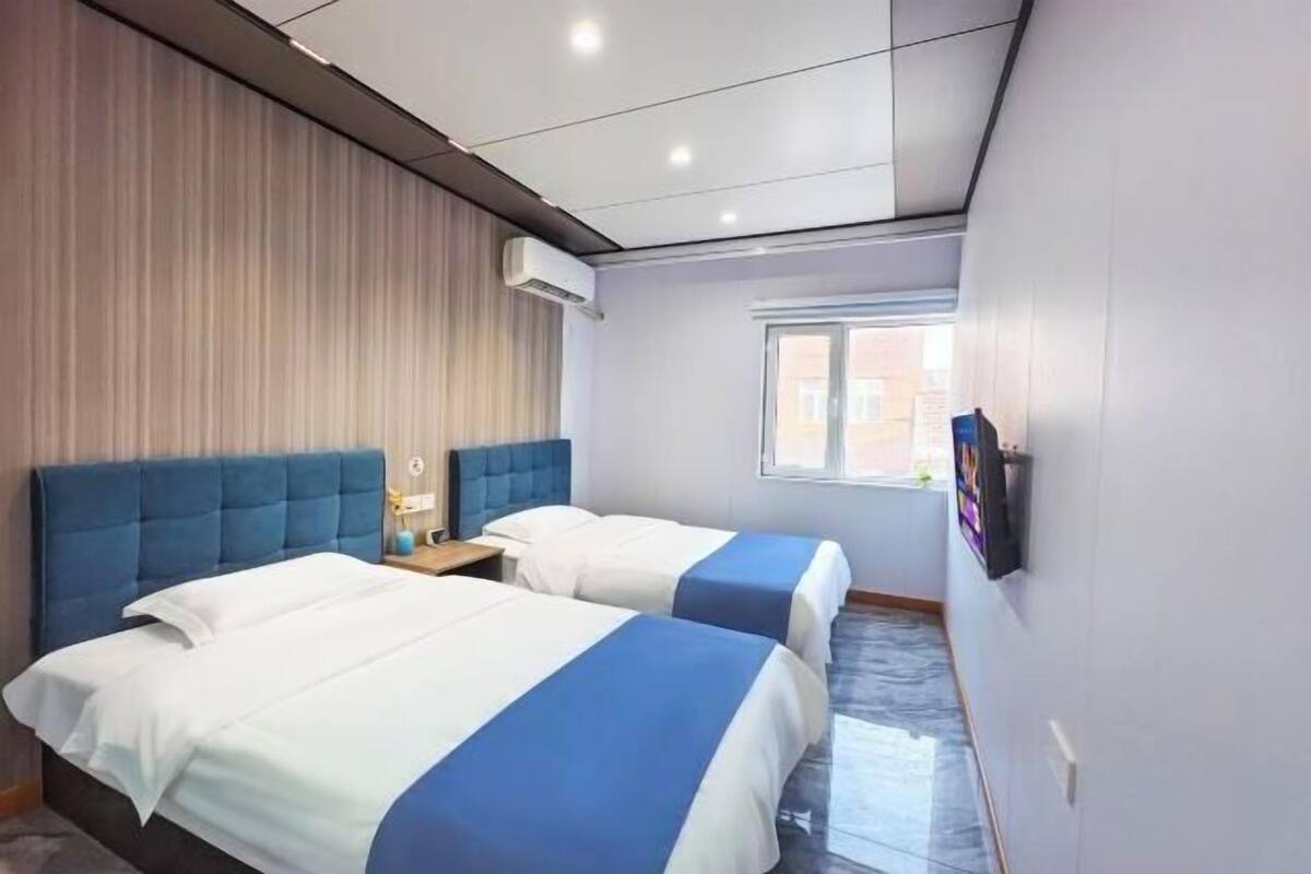 A hotel room with two beds, a window, and a wall-mounted TV.