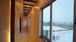 A corridor with a large window, a marble floor, and a view of the rooftop. - Lipi Resort and Spa (Kanthi)