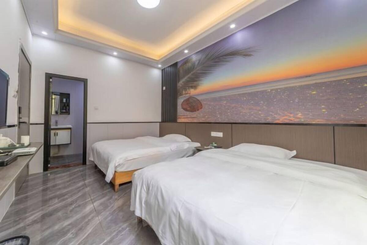 A hotel room with two beds, a desk with a chair, a mirror, and a cityscape mural on the wall.