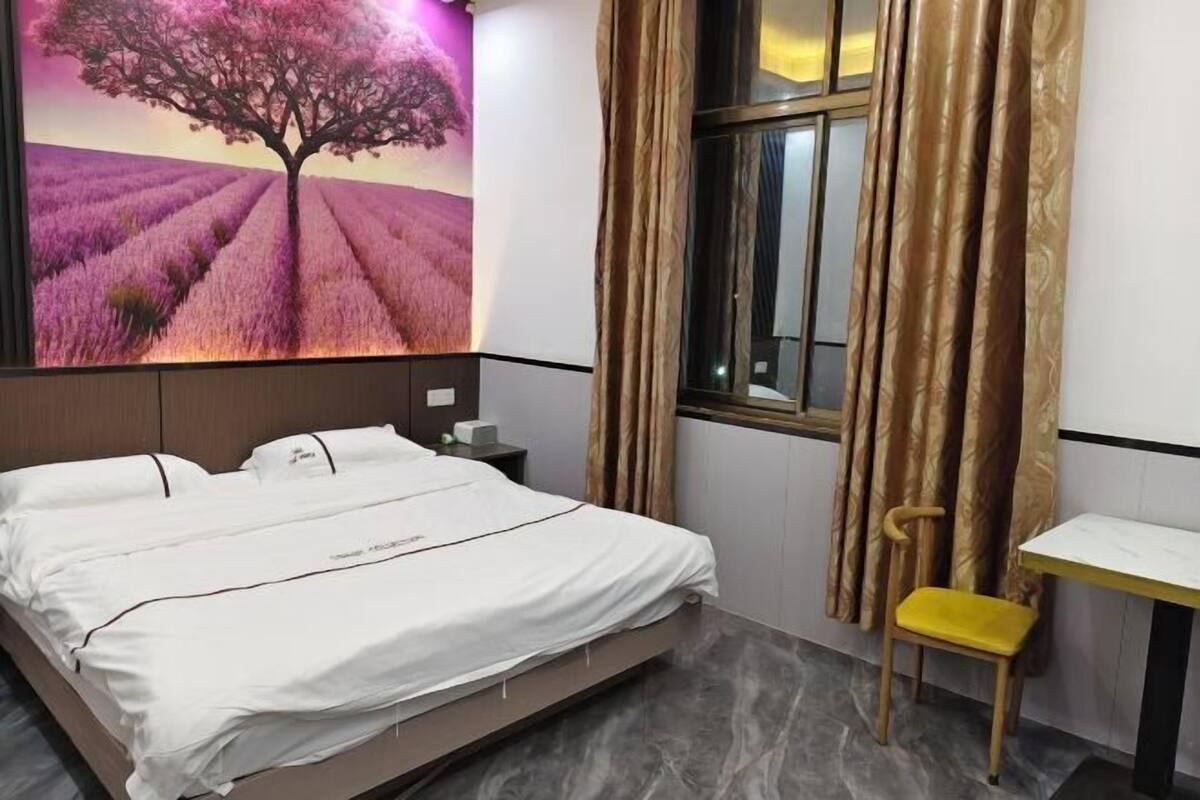 A bedroom with a bed, a nightstand, a chair, a window with curtains, and a wall with a lavender field mural.