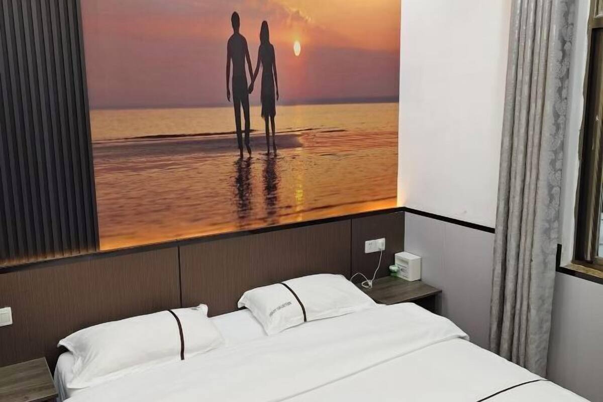 A hotel room with a bed, a nightstand, a wall-mounted TV, and a window with curtains.