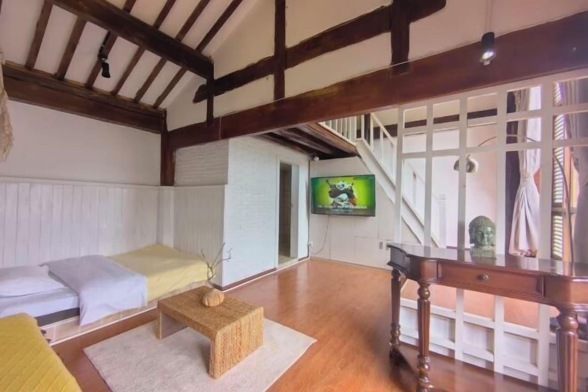 Una habitación con una cama, una mesita, un televisor y una escalera.