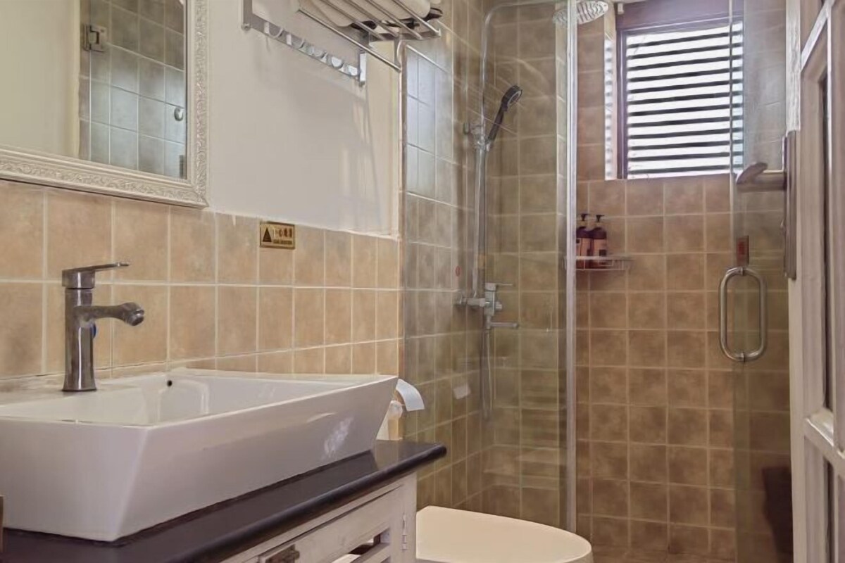 A bathroom with a white sink, a mirror, a shower, and a toilet.