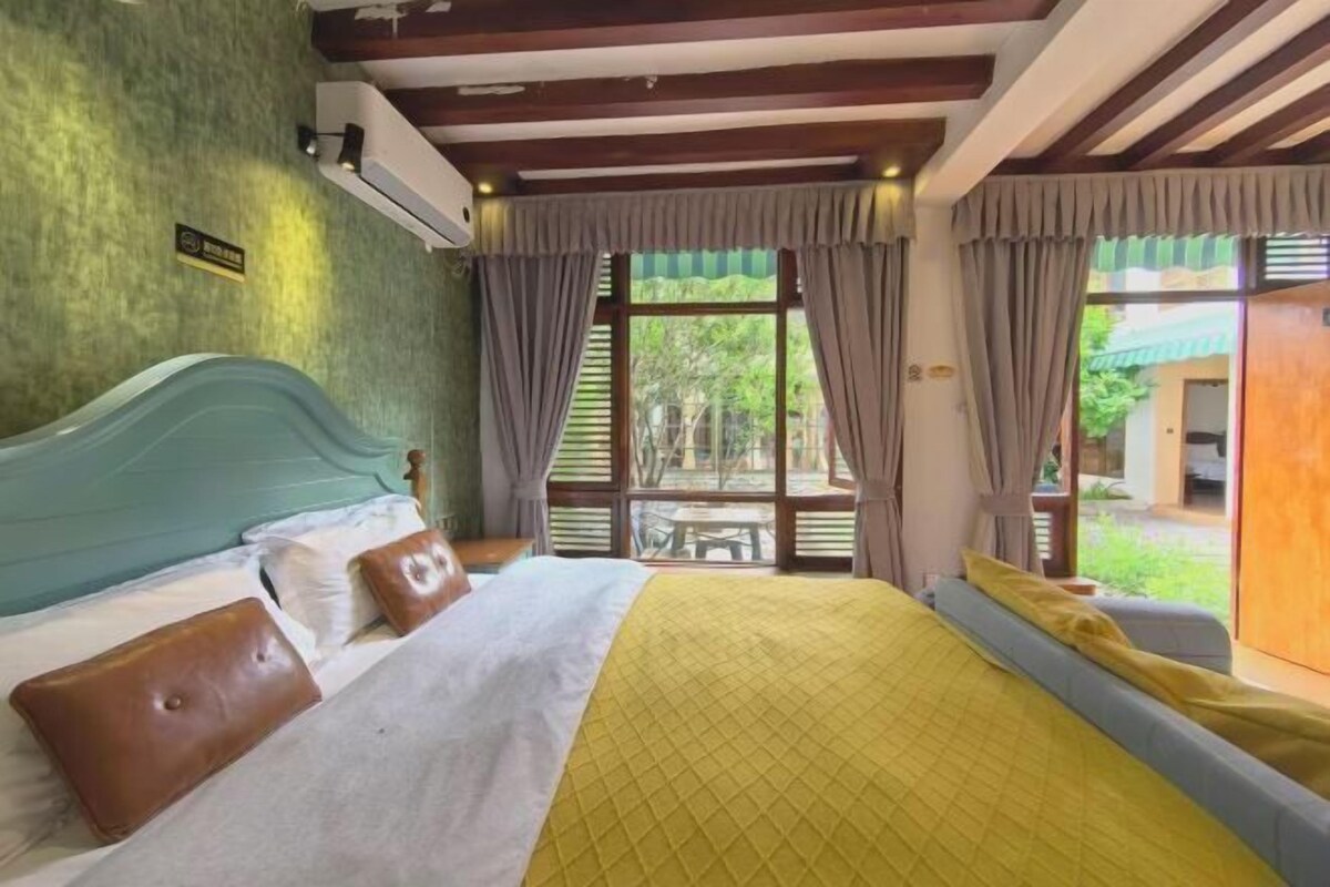 A bedroom with a bed, curtains, and a view of the outdoors.