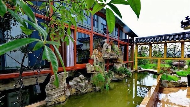 A traditional building with a water feature, stone structures, and greenery. - Junchen Business Hotel (Chongqing)