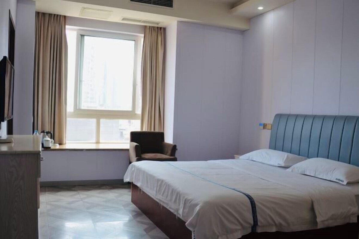 A hotel room with a bed, a chair, a window, and a television.