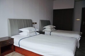 A hotel room with two single beds, a wooden nightstand, and a dark closet. - Junchen Business Hotel (Chongqing)