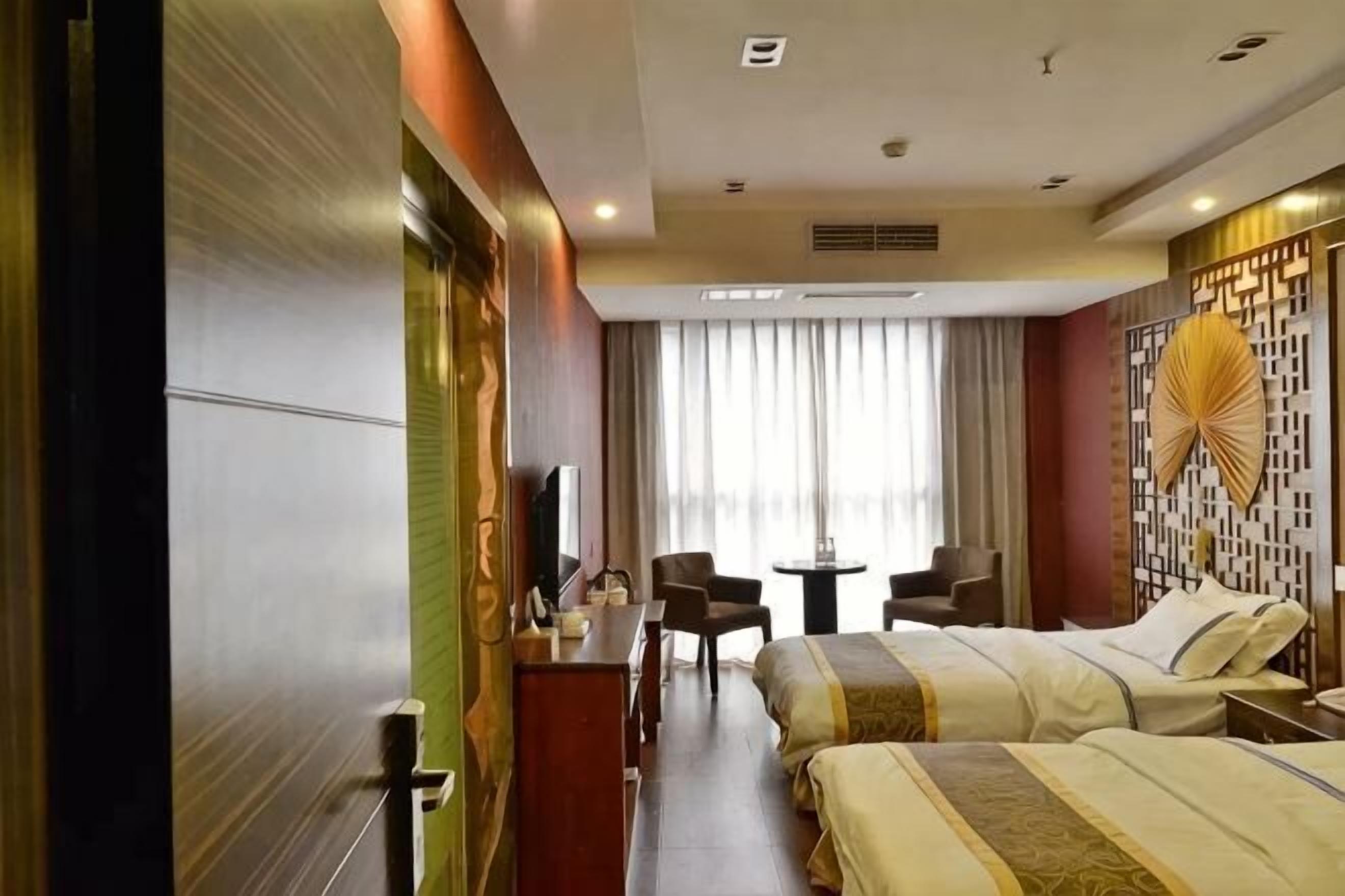 Hotellihuone, jossa on kaksi sänkyä, työpöytä, tuoli, televisio ja ikkuna, jossa on verhot.