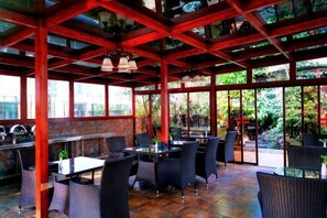 Um restaurante ao ar livre com mesas e cadeiras, teto vermelho e grandes janelas.