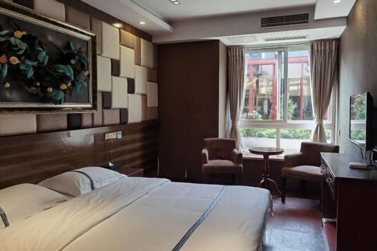 A hotel room with a large bed, two chairs, a small table, a TV, and a window with curtains.