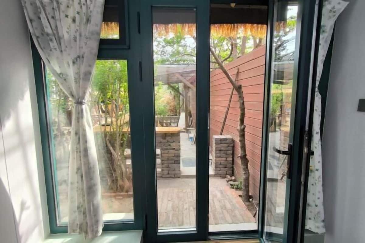 Une pièce dotée d’une porte-fenêtre coulissante donnant sur un patio extérieur, avec un mur en briques et un petit arbre.