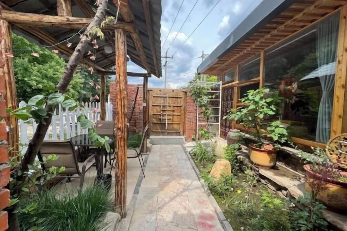 Un espace extérieur rustique agrémenté d’une pergola en bois, d’une clôture blanche en piquets et d’un mur en briques.