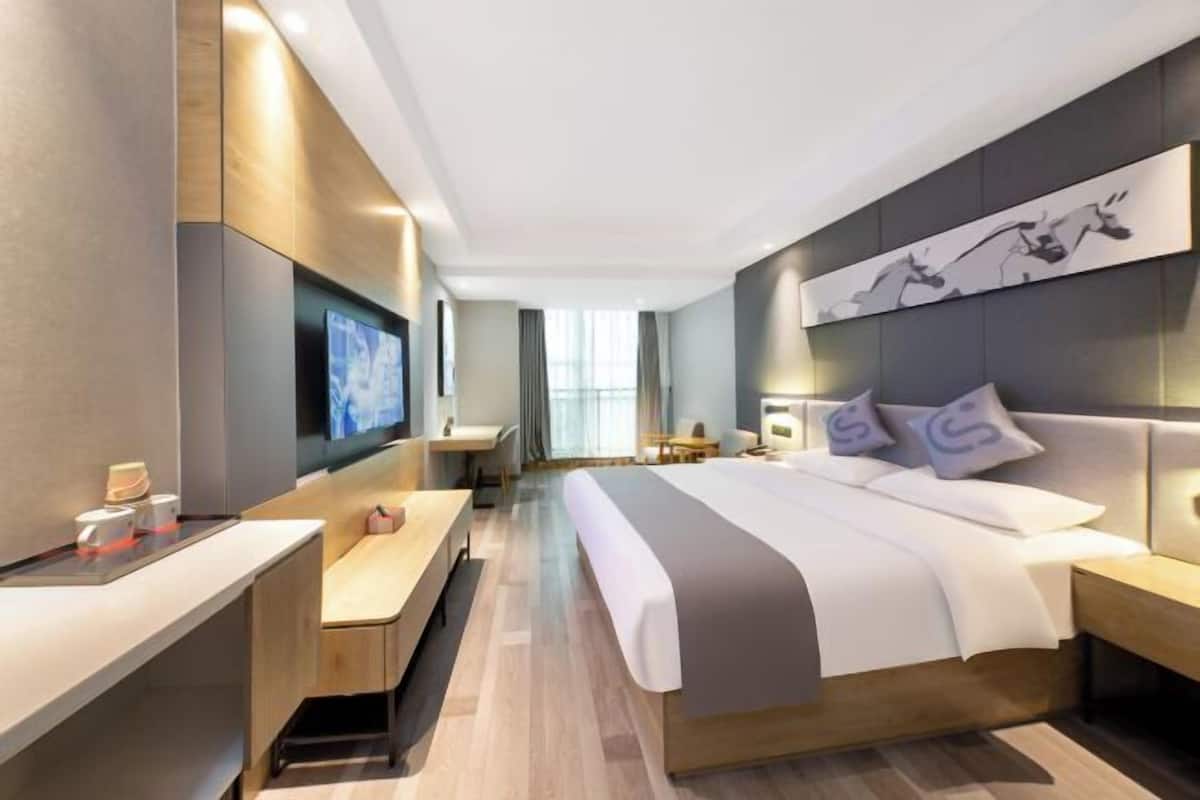 A modern hotel room with a large bed, a desk, and a TV.