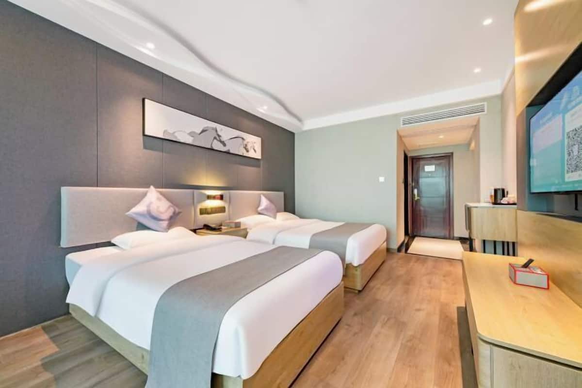 A hotel room with two beds, a desk, a TV, and a door leading to a bathroom.