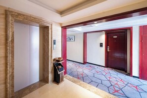 A hotel corridor with a patterned carpet, a coat check, and a door with a red frame. - Yayue Hotel (Yongxin Central Plaza) (Yongxin)