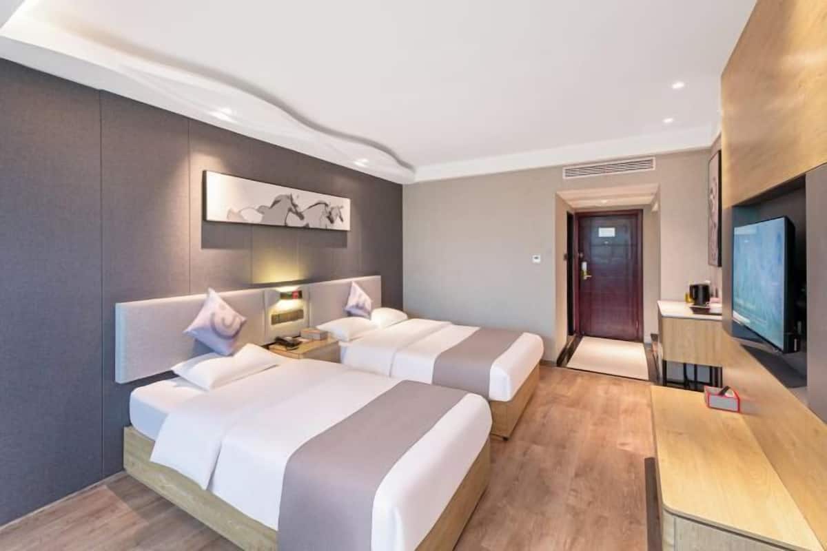 A modern hotel room with two beds, a desk, a TV, and a painting on the wall.