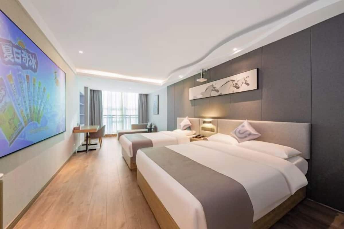 A hotel room with two beds, a desk, a chair, a large wall-mounted TV, and a painting.