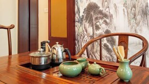 A wooden dining table with green teapots and a metal teapot, set against a backdrop of a traditional Chinese landscape painting. - Yayue Hotel (Yongxin Central Plaza) (Yongxin)