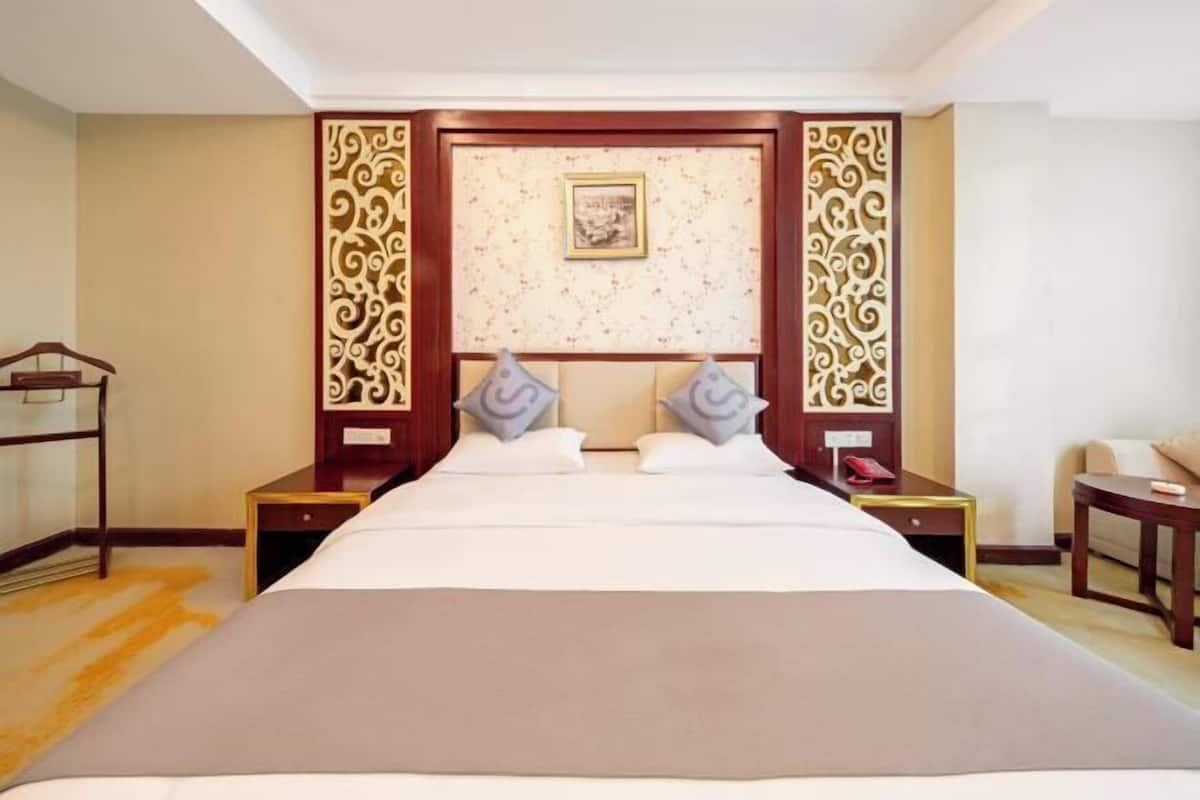 A hotel room with a large bed, two nightstands, a wooden headboard, and a decorative wall panel.