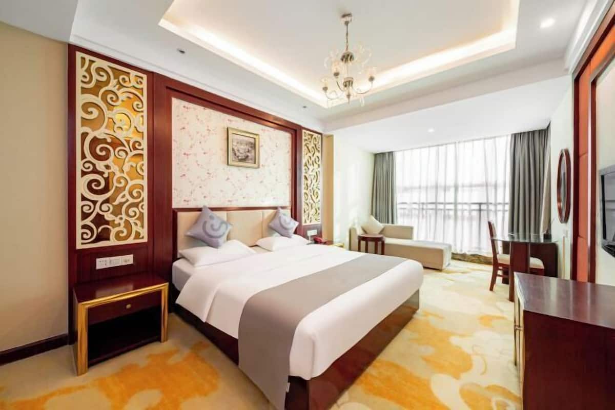A hotel room with a large bed, a desk, a chair, a television, and a window with curtains.