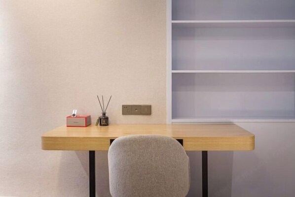 A minimalist room with a wooden desk, a chair, a red box, a small vase with reeds, and a wall-mounted switch.