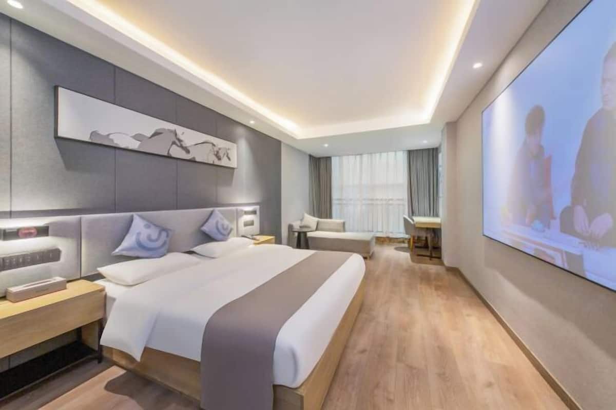 A modern hotel room with a large bed, bedside tables, a TV, and a seating area with a chair and a small table.