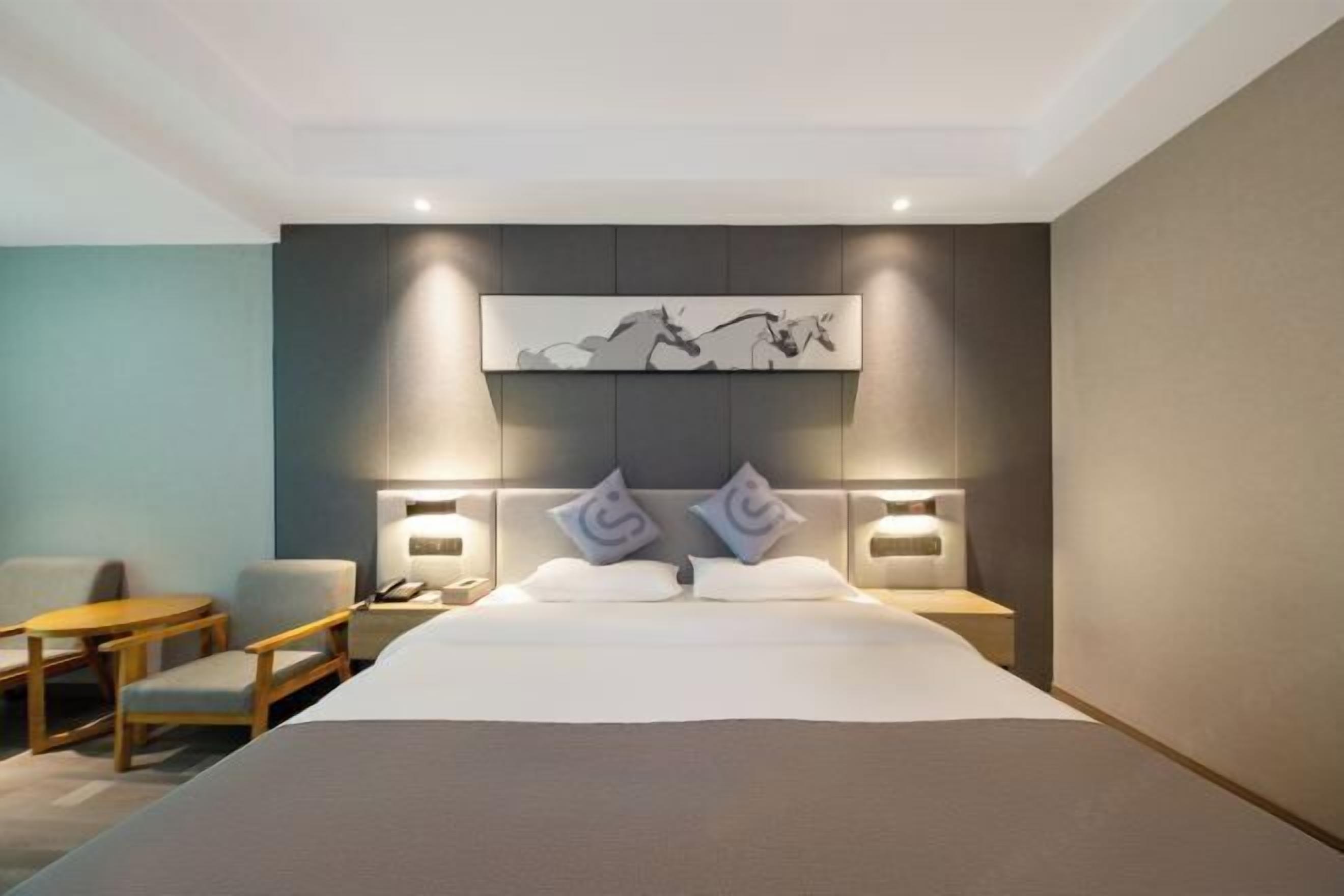 A modern hotel room with a large bed, a bedside table, a chair, and a small table.