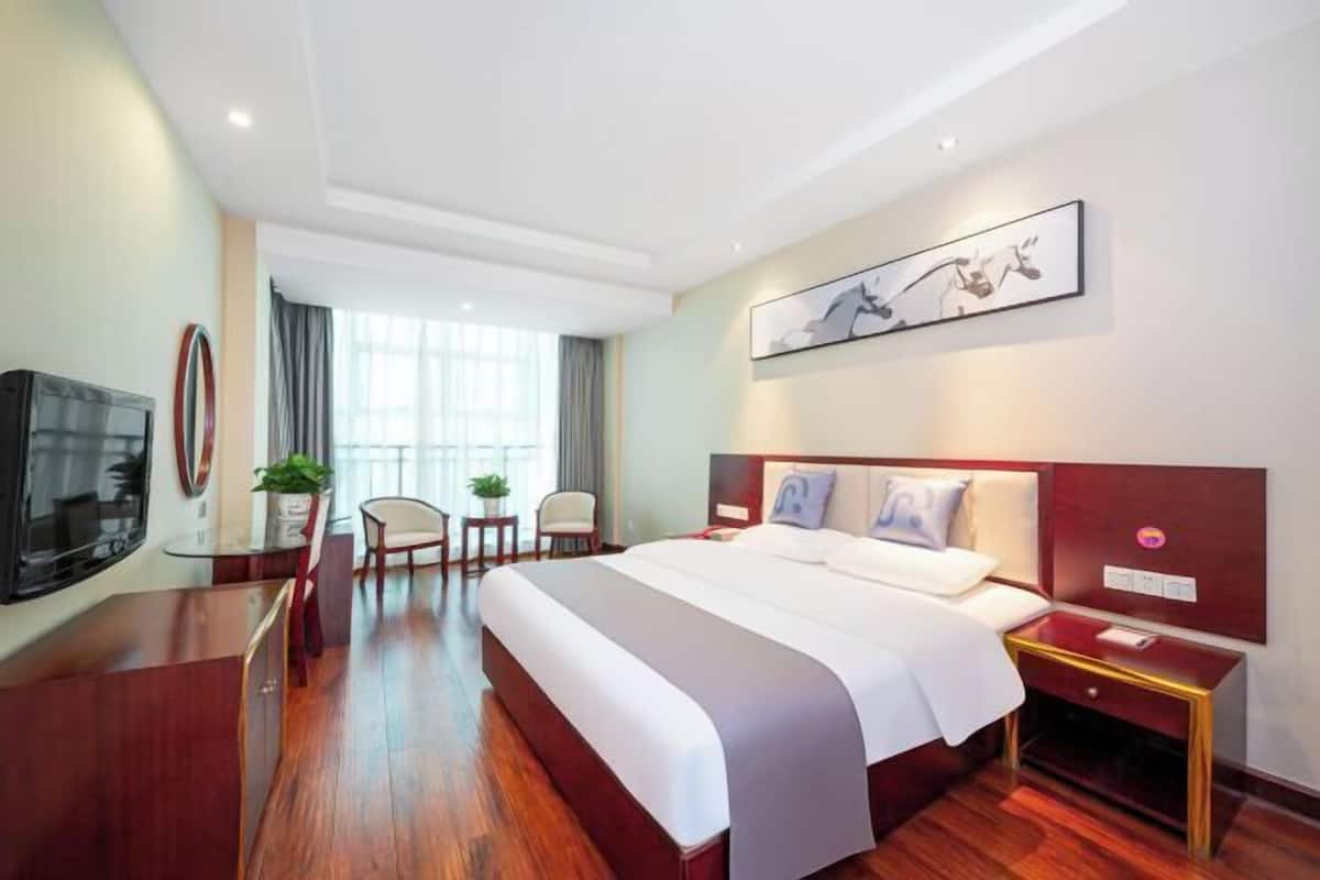 A hotel room with a large bed, a TV, a desk, and a window with curtains.
