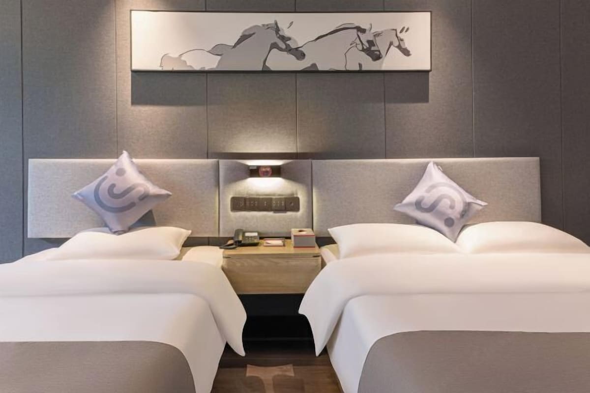 A hotel room with two beds, a nightstand, a phone, and a wall-mounted artwork.