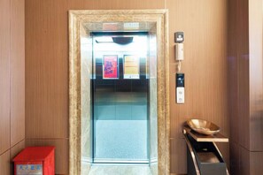 Un ascensor con marco de mármol, una caja roja y una bandeja de madera con un bol.