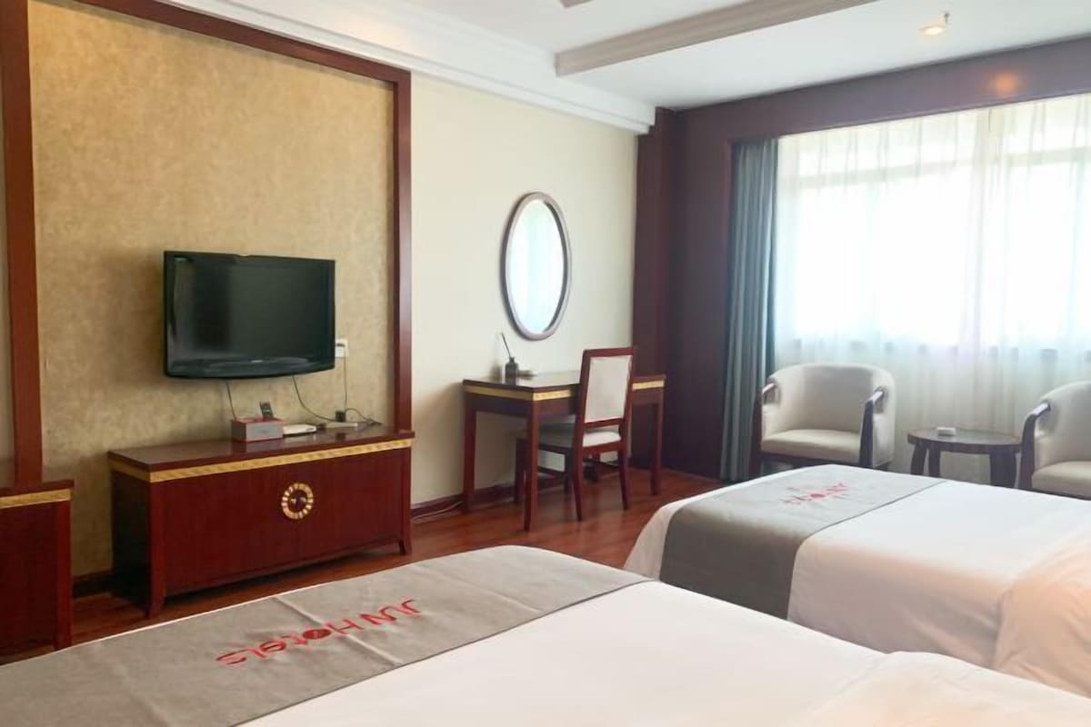 A hotel room with two beds, a TV, a desk with a chair, and a window with curtains.