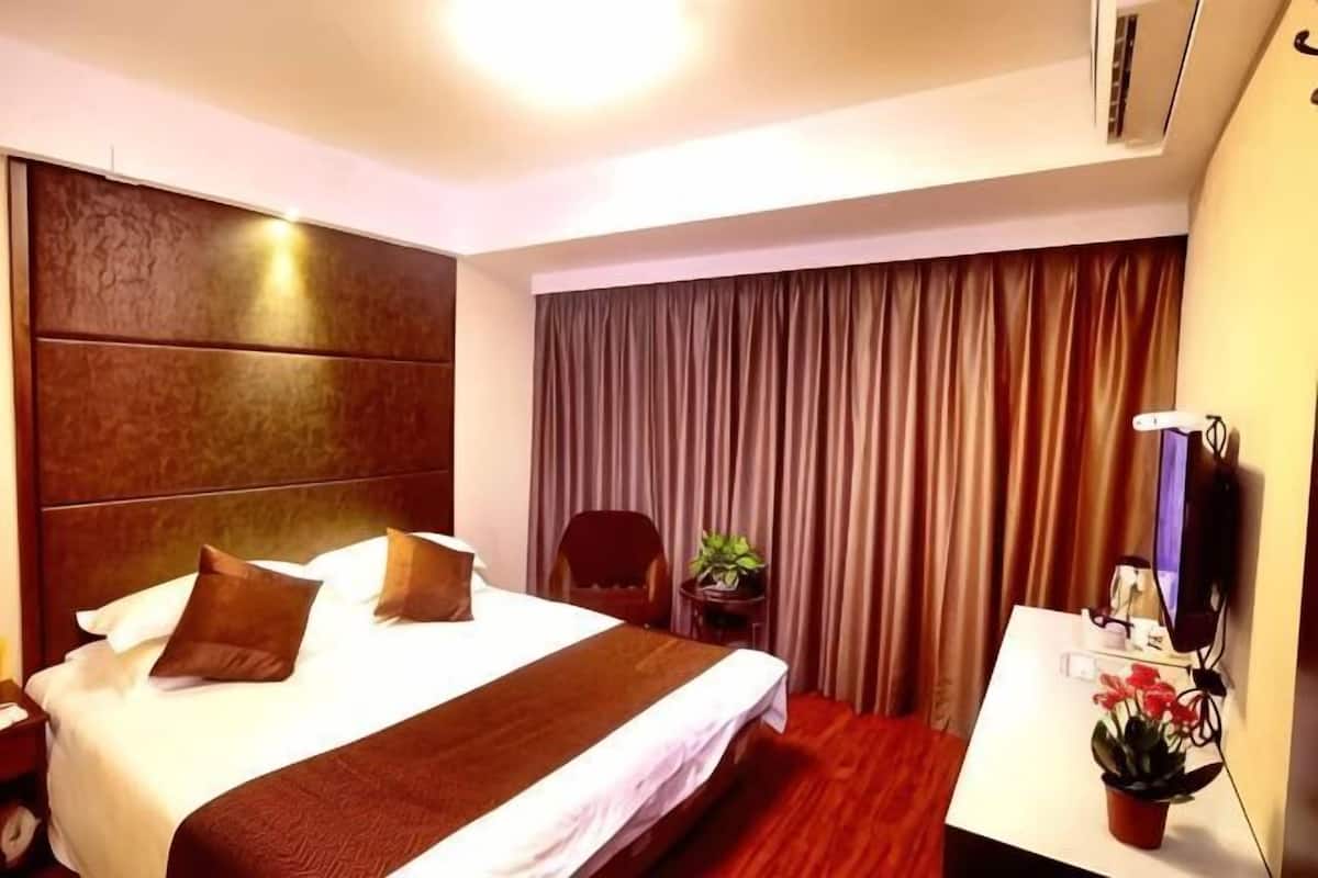 A hotel room with a large bed, a desk with a plant, and a curtain-covered window.