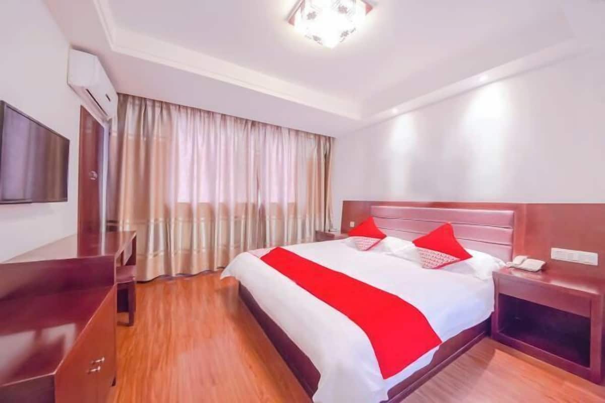 A hotel room with a large bed, a bedside table, a TV, and a window with curtains.