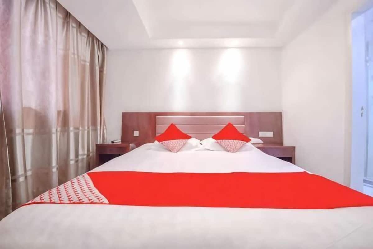 A hotel room with a large bed, a wooden headboard, a nightstand, and a window with curtains.