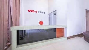 Un mostrador de recepción con una mampara de vidrio, un logotipo rojo y un letrero con caracteres chinos.