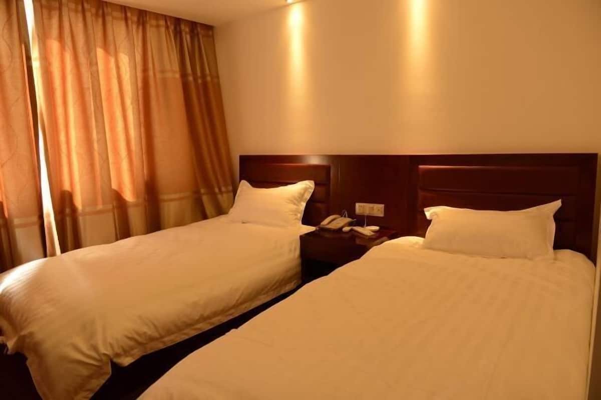 A hotel room with two single beds, a bedside table with a phone, and a window with curtains.