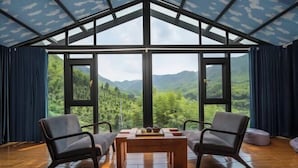 Une pièce dotée d’une grande fenêtre, de deux chaises, d’une table et offrant une vue sur les montagnes.