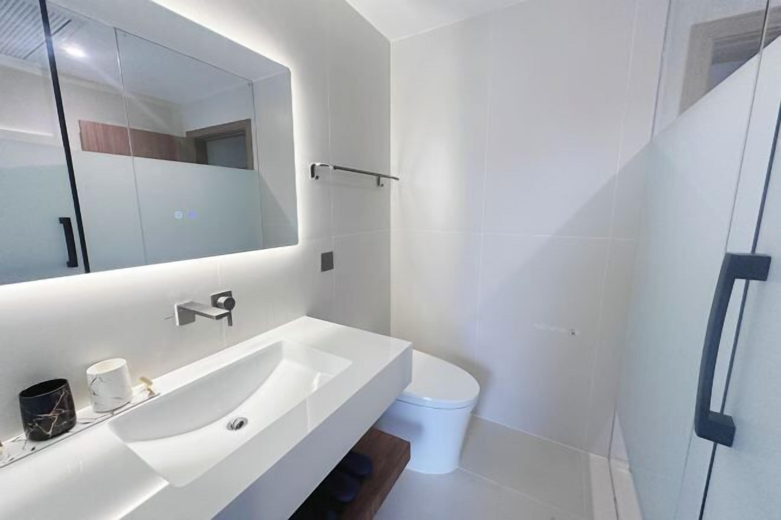 A modern bathroom with a large mirror, a white sink, and a toilet.