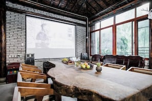 A conference room with a large wooden table, chairs, a projector screen, and a brick wall. - Anji Dongsha Lake Farm Stay (Anji)