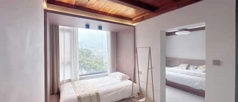 A bedroom with a large window, a bed, a wardrobe, and a ceiling with exposed beams.